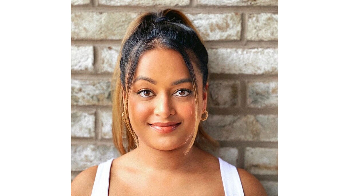 A headshot image of Krishni Rajah smiling for the photo standing in front of a brick wall.