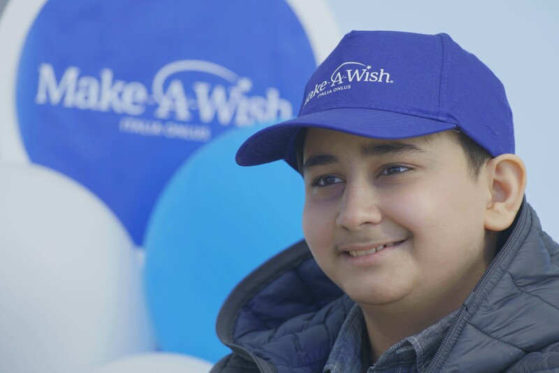 Hadi, uno dei bambini che hanno visto un desiderio realizzato grazie a Make-A-Wish, sorridente con un cappellino blu Make-a-Wish