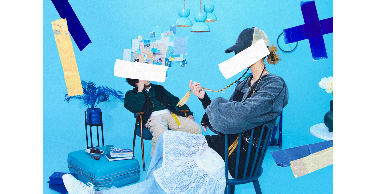 水色の背景、水色と青を基調にした家具が配置され、3人の人物が青い椅子に座っている。2人とも顔の部分が白いテープで隠されている。