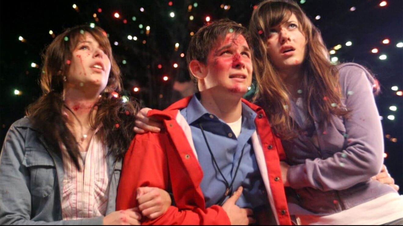 Three teenagers looking upward at holiday lights with terrified expression