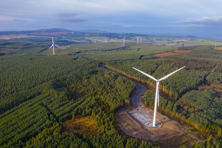 Windräder in einer hügeligen Landschaft mit grünem Wald