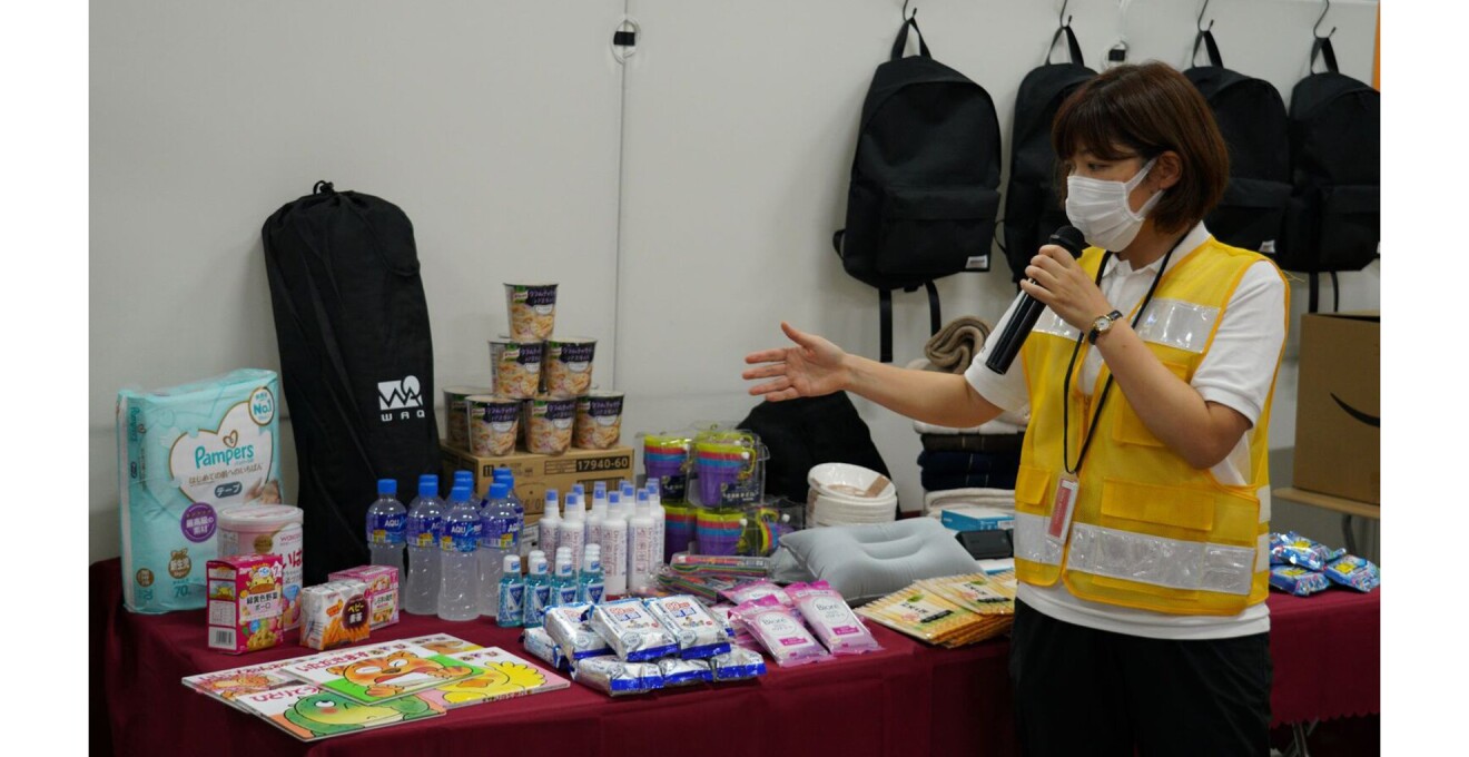 ベビー用品、食料品、日用品、衛生用品など並べられた災害物資の説明をしている写真