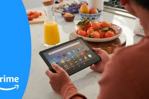 A man sits at a kitchen counter looking at his Fire Tablet, with orange juice and a bowl of tomatoes right in front of him.