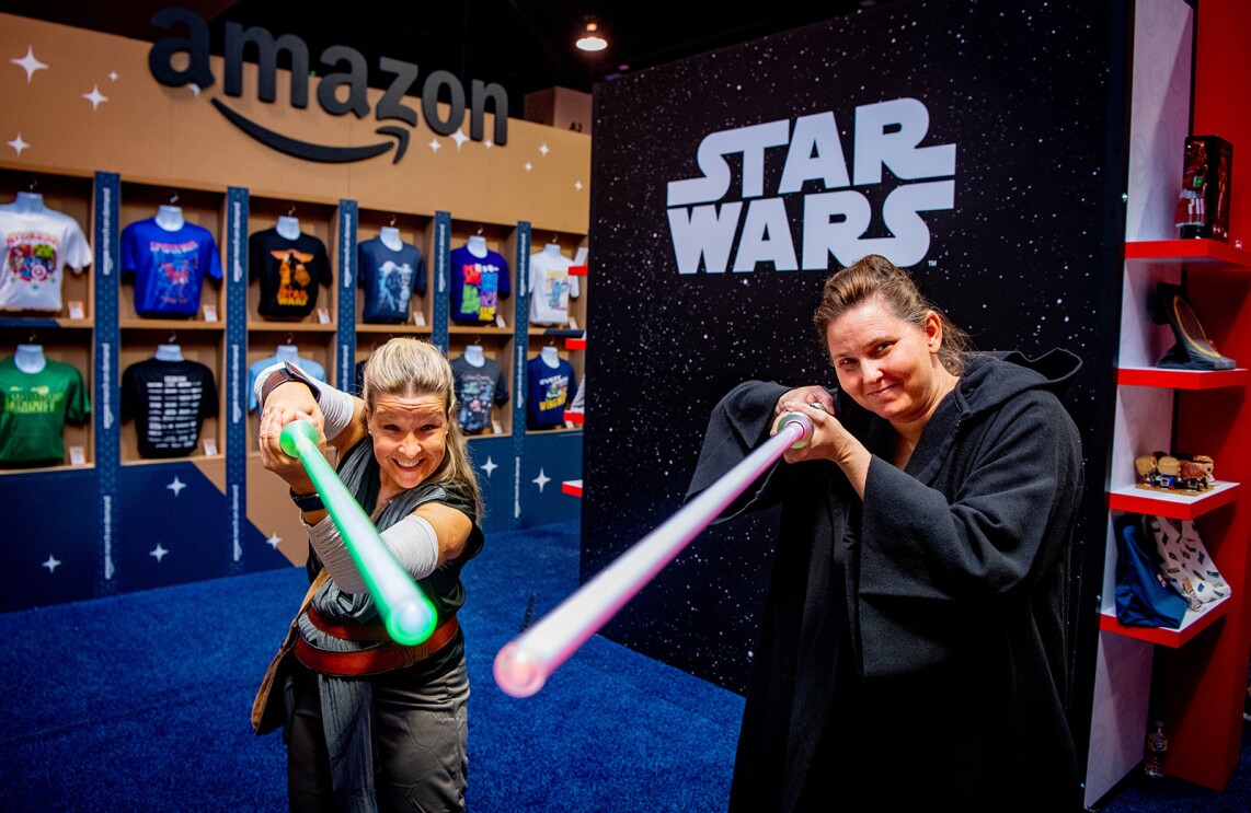 Two women smile for a photo holding light sabers at the camera