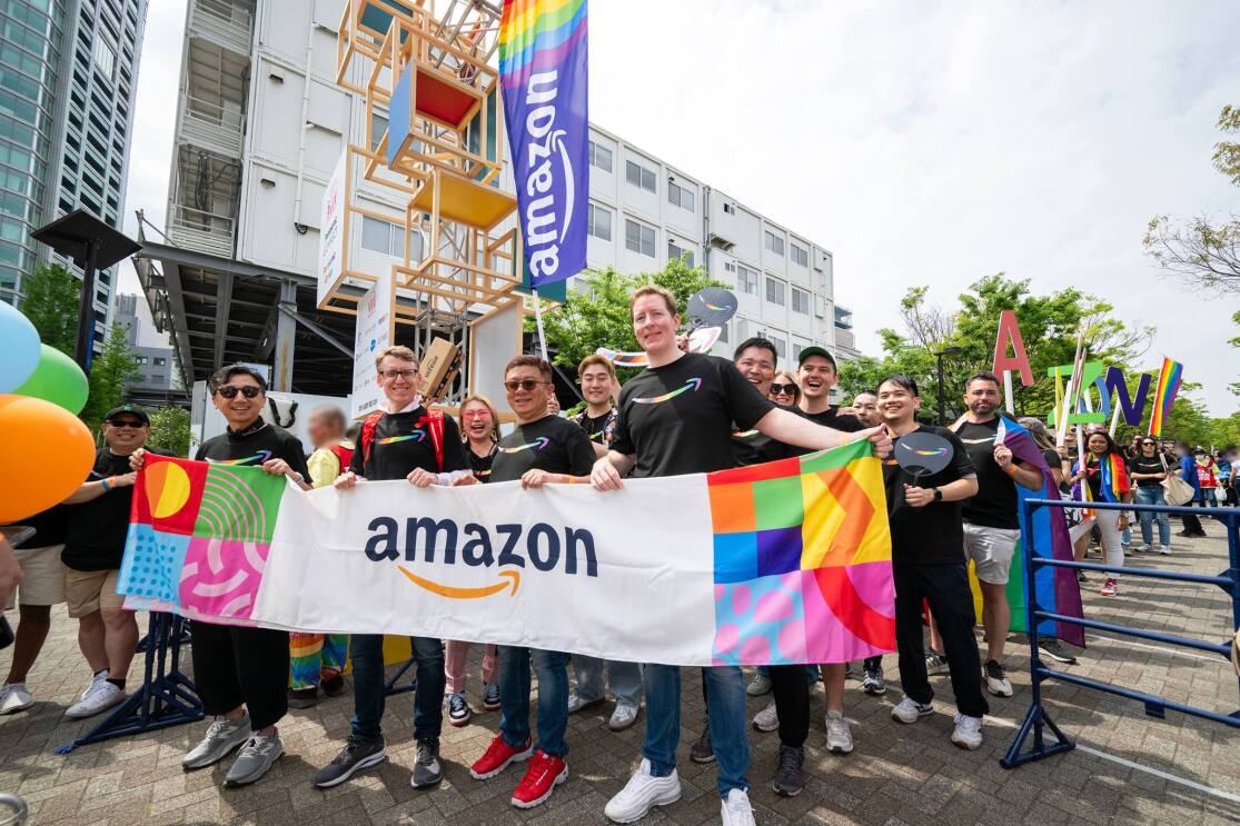 4人の男性がAmazonのロゴが入った横断幕を持っている。彼らの後ろには多数の人々が集まっている