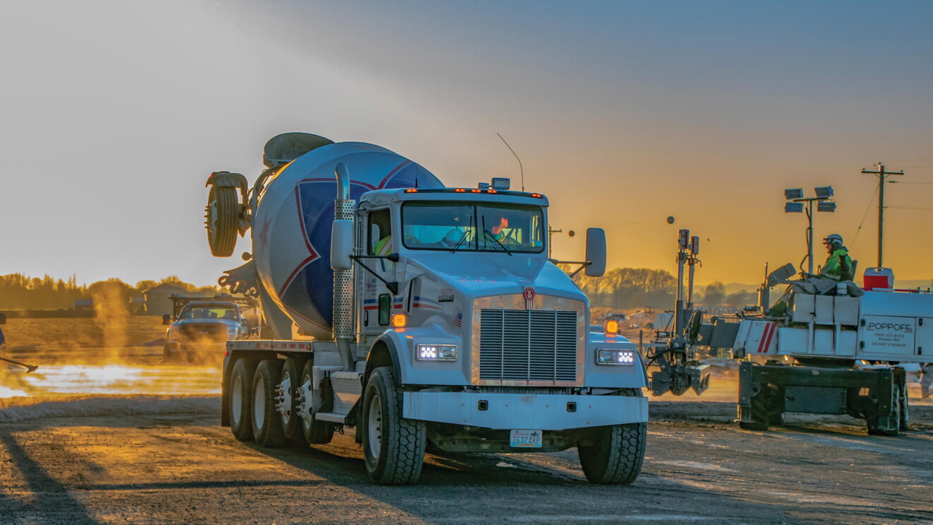 An image of a concrete truck on a construction field with a sunset in the background. 