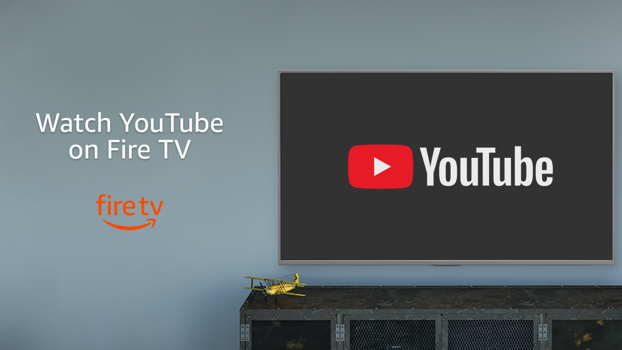 En una pared gris aparece un tlevisor con el logo de YouTube. Debajo del televisor un mueble de color gris más oscuro con una avioneta de color amarillo. En el lado izquierdo de la imagen la frase Watch YouTube on Fire TV.