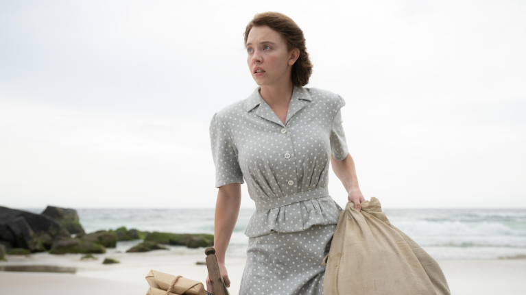 Woman in 1950s polka dot dress on beach with luggage