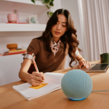Echo Dot on desk with girl in background writing on paper