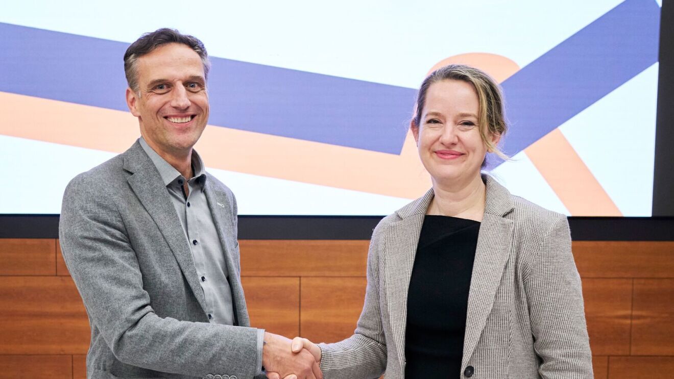 Representatives from Amazon and IOM sign an agreement and shake hands.