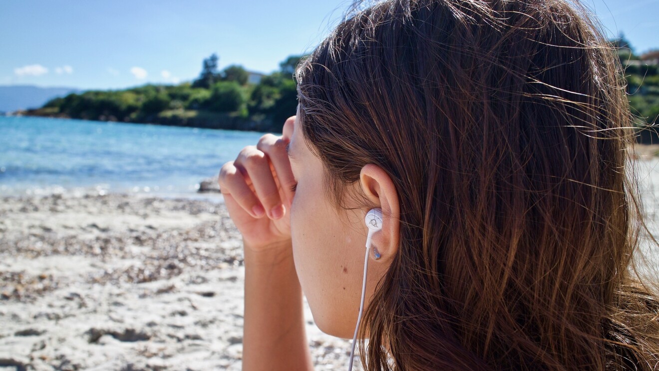 A girl listening wearing headphones and sitting on a beach