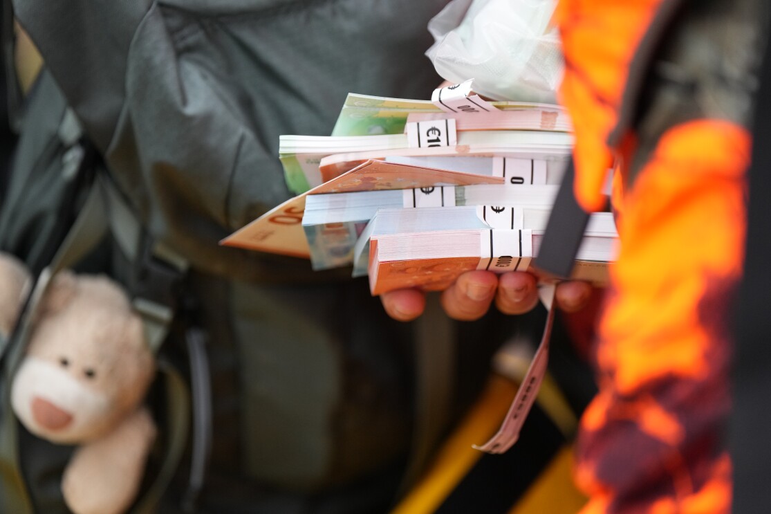 Bargeld in einer Hand mit einem Teddybär im Rucksack. 