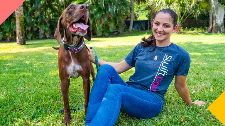 A photo of Swift Paws founder & CEO Meghan Wolfgram sitting in the grass at a park with a dog.