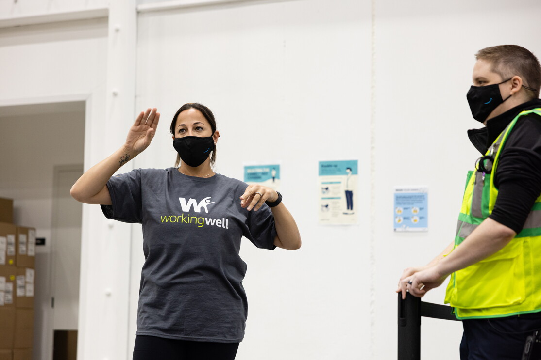 An image of Leila Brown wearing WorkingWell shirt and a mask with the Amazon logo on it as she speaks to employees in her fulfillment center.
