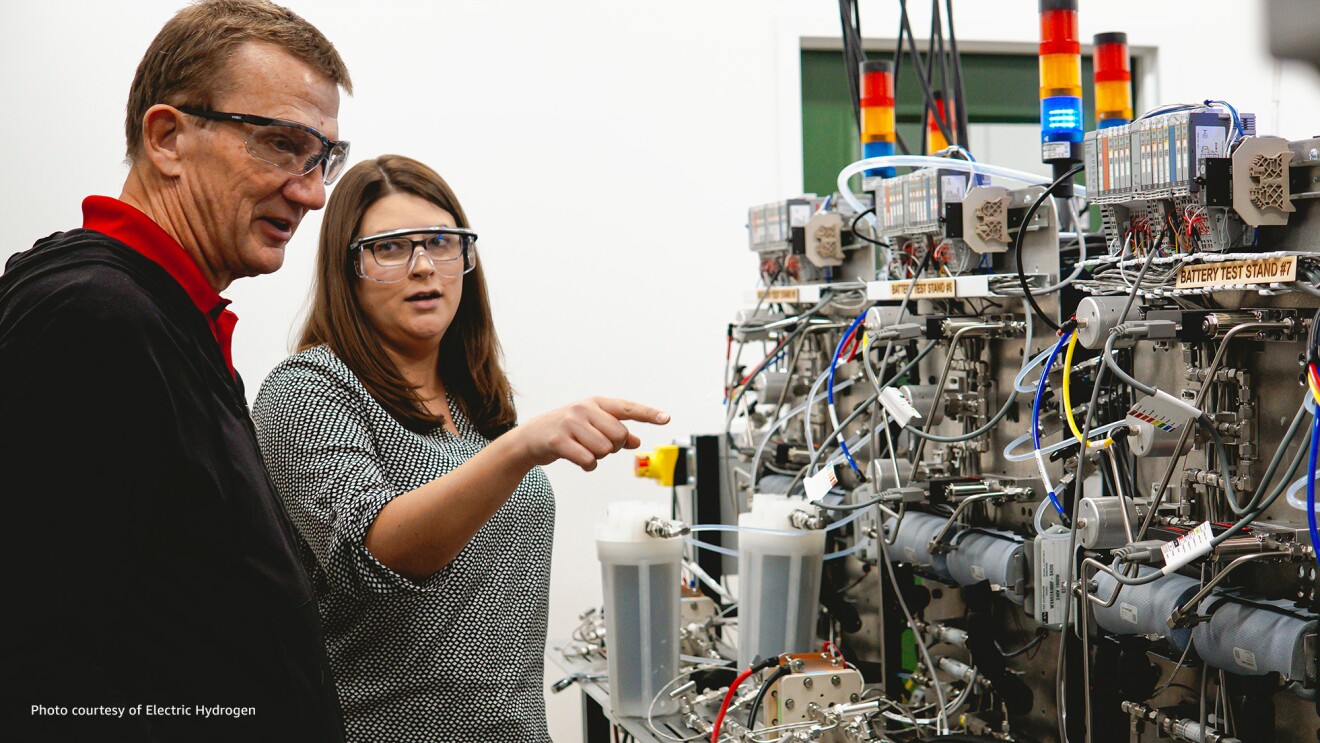 Two people wear safety glasses as they look at the inner workings of a machine.