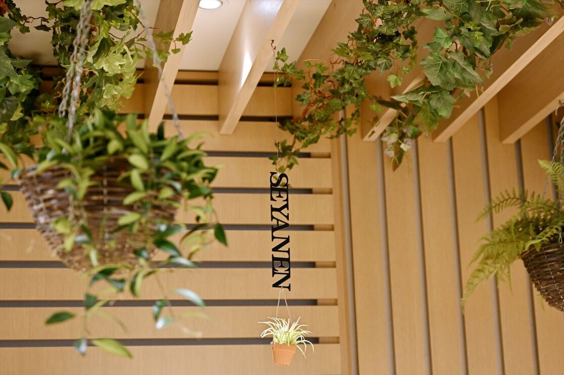 木のパネルで作られた壁の前にアルファベットの文字で「SEYANEN」が天井から吊り下げられている