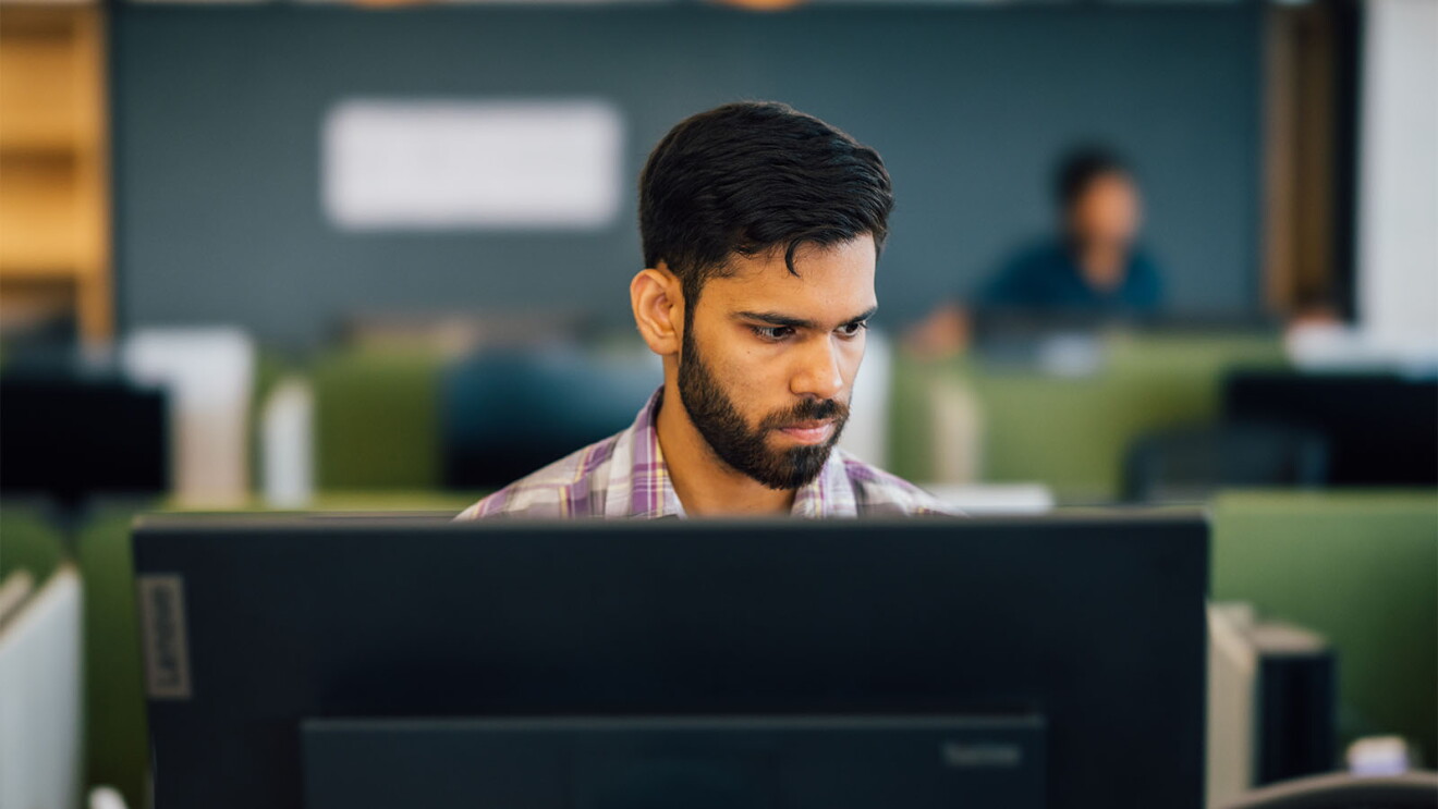 Man with beard working intently at desktop computer in modern office