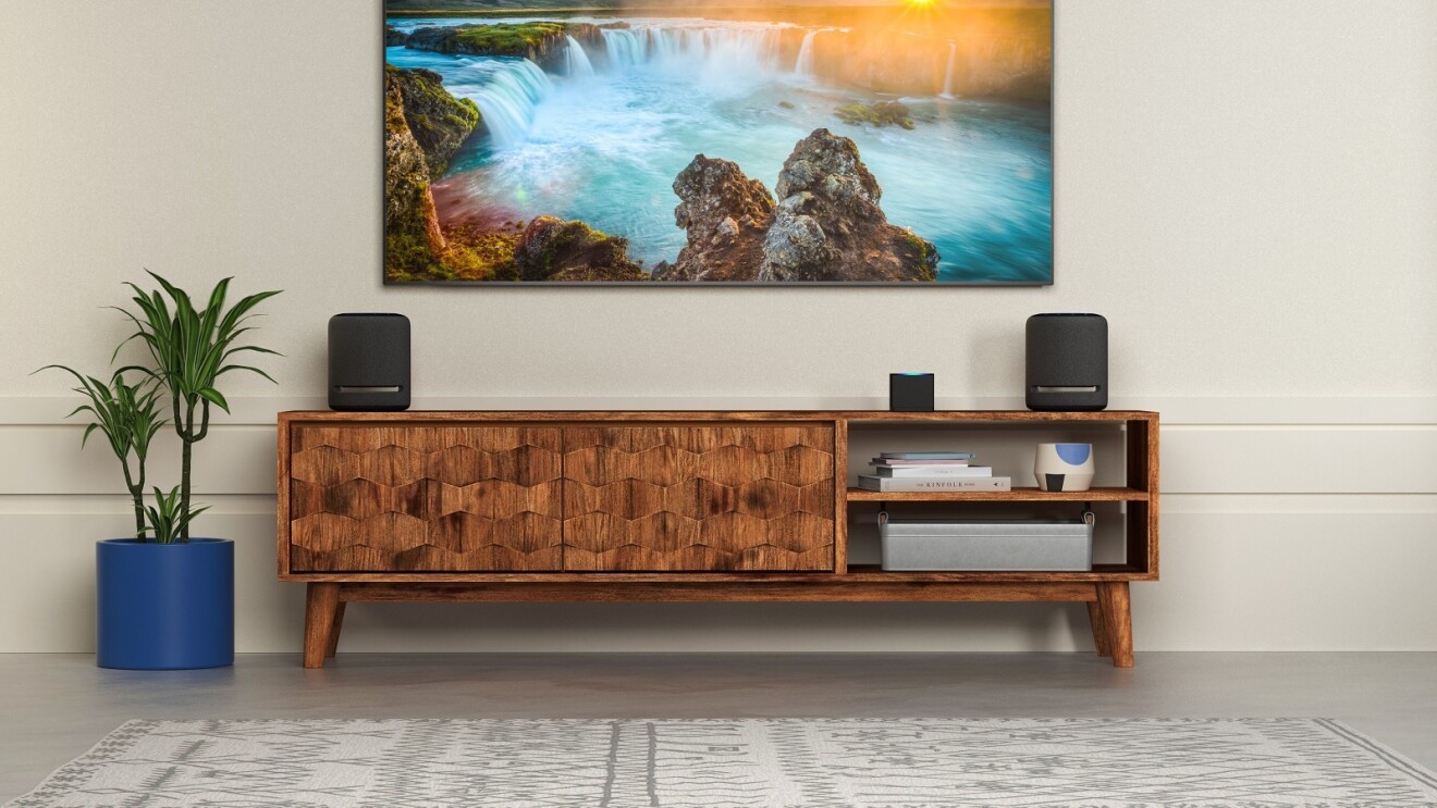 Amazon Fire TV Cube und Amazon Echo Studio stehen auf einem Sideboard unter einem Fernseher