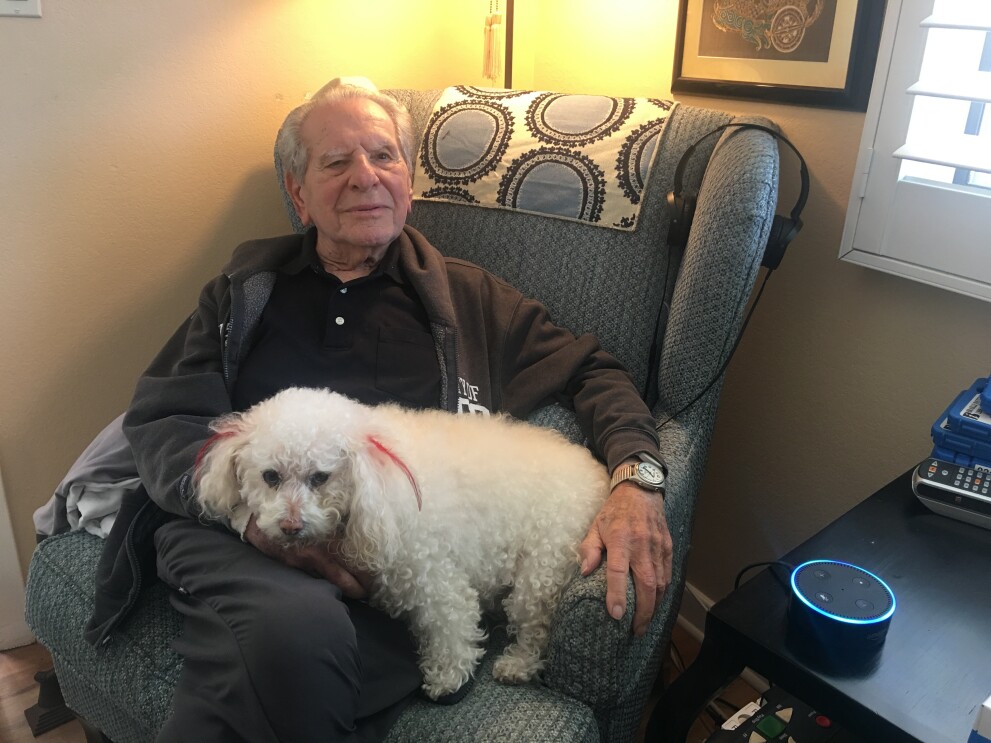 A man sits in an easy chair with his dog resting on his lap.
