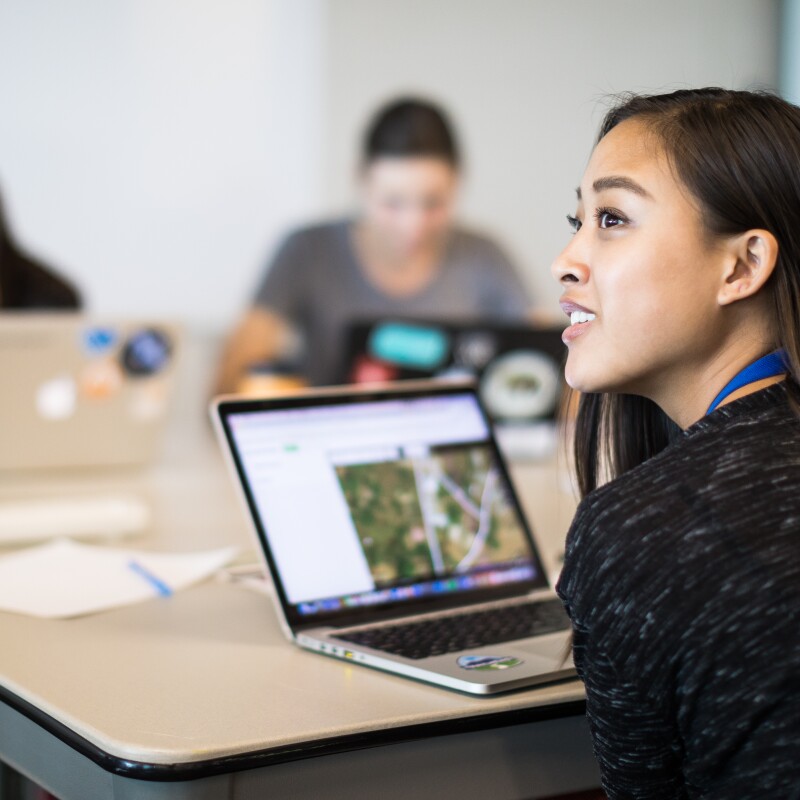 A young woman works at a computer in a pre-COVID-19 training session, in front of her, two other individuals are also working on their laptop computers