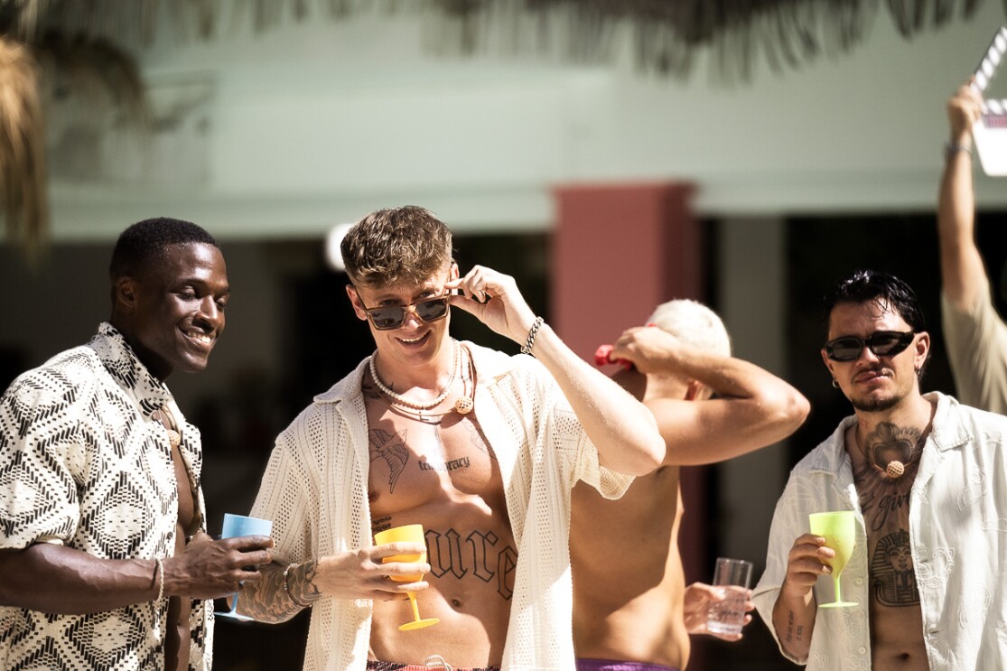Eine bunte Gruppe junger Männer genießt Getränke bei einer sonnigen Party im Freien.