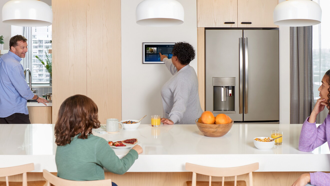 Family gathering in modern kitchen with smart Alexa display mounted on wall