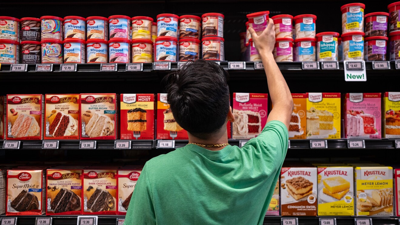 A photo of a customer reaching for a frosting container on a shelf inside an Amazon Fresh store.