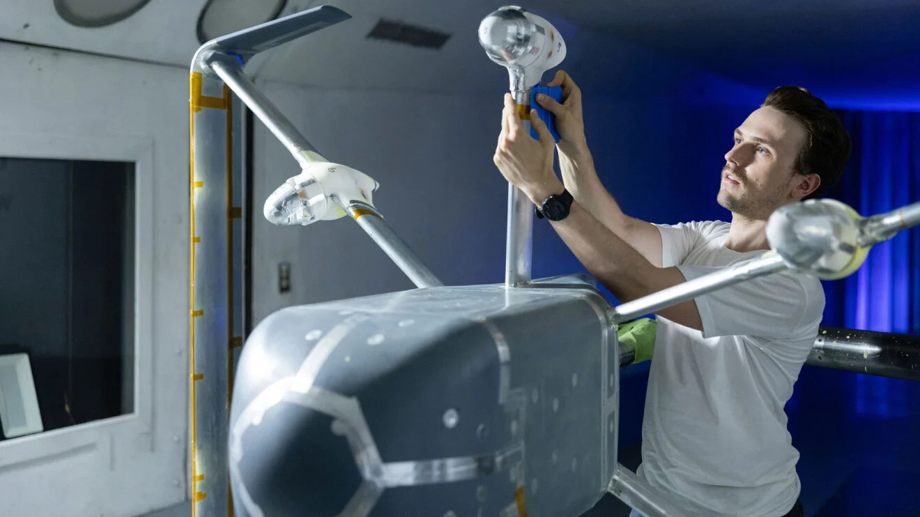 Un tecnico in maglietta bianca sta svolgendo operazioni di manutenzione su un grande drone Amazon all'interno di un laboratorio 
