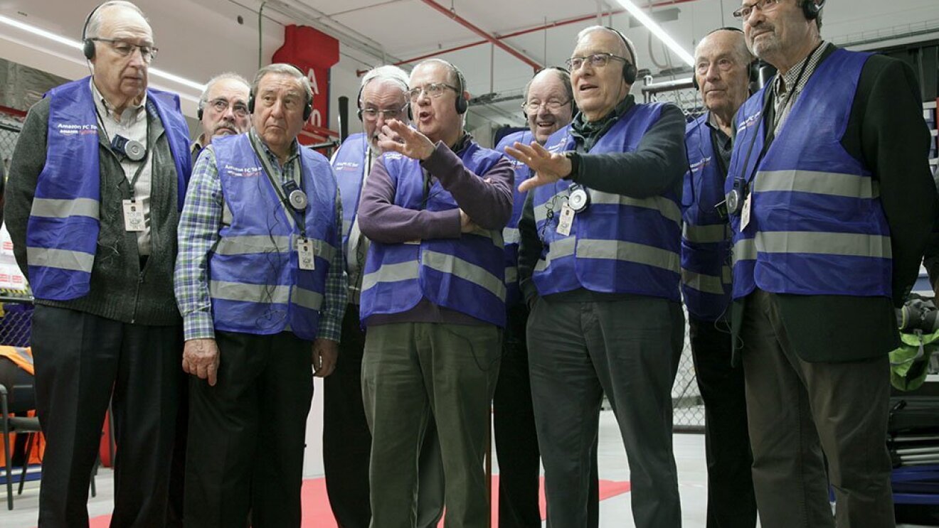 Un grupo de ingenieros jubilados durante una visita al centro logístico. Todos ellos visten con chaleco azul.