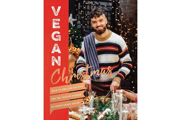 Vegan Christmas cookbook features a man wearing a sweater, with a dish towel thrown over his shoulder, carving into a dish. On either side of him are guests at his table, appearing to enjoy a holiday meal.