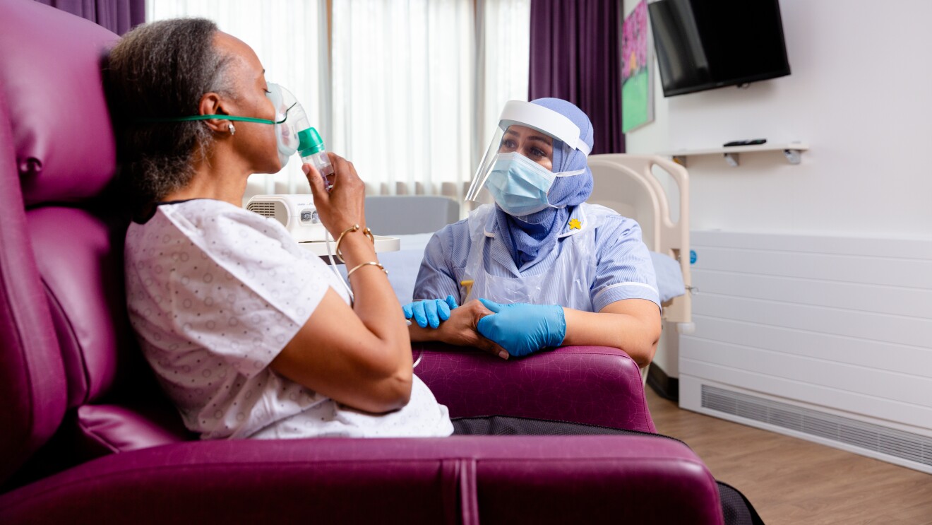 NHS carer in PPE and patient sitting in chair with oxygen mask