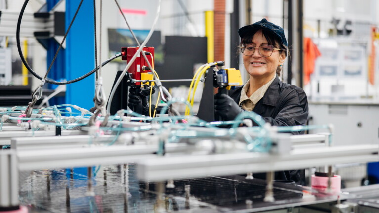 Female fulfillment center worker smiling while operating manufacturing equipment with robotic arms