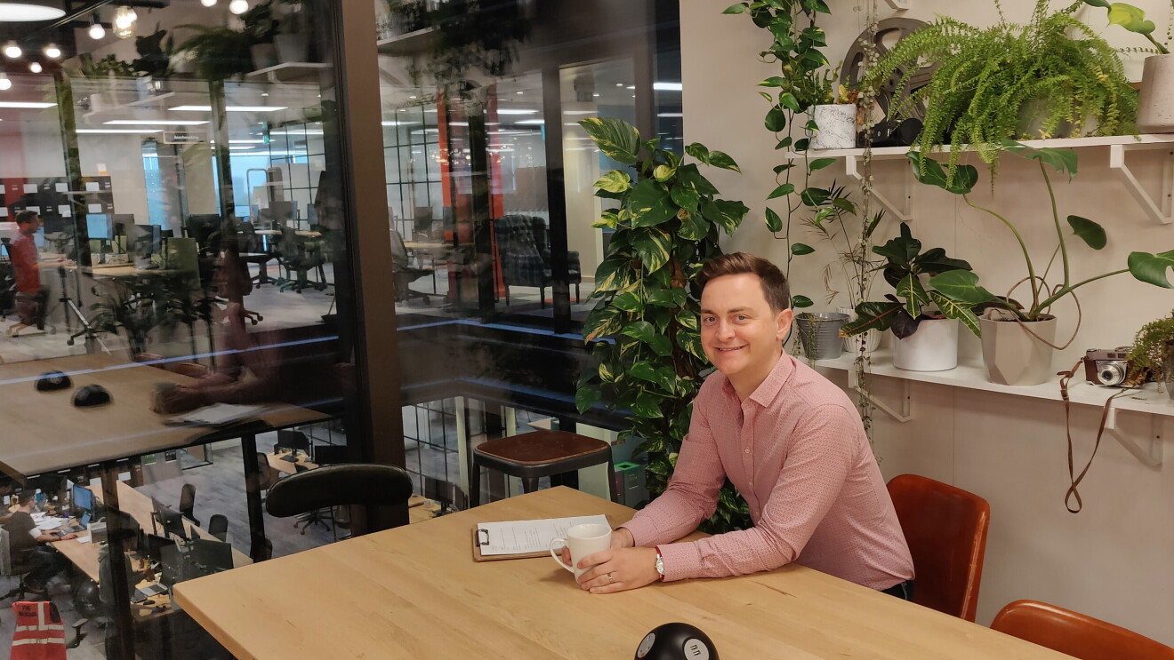 Dave Brittain smiling and sat at a desk in Amazon head office 