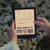 Mains tenant une liseuse Kindle affichant une interface en français sur fond de marguerites