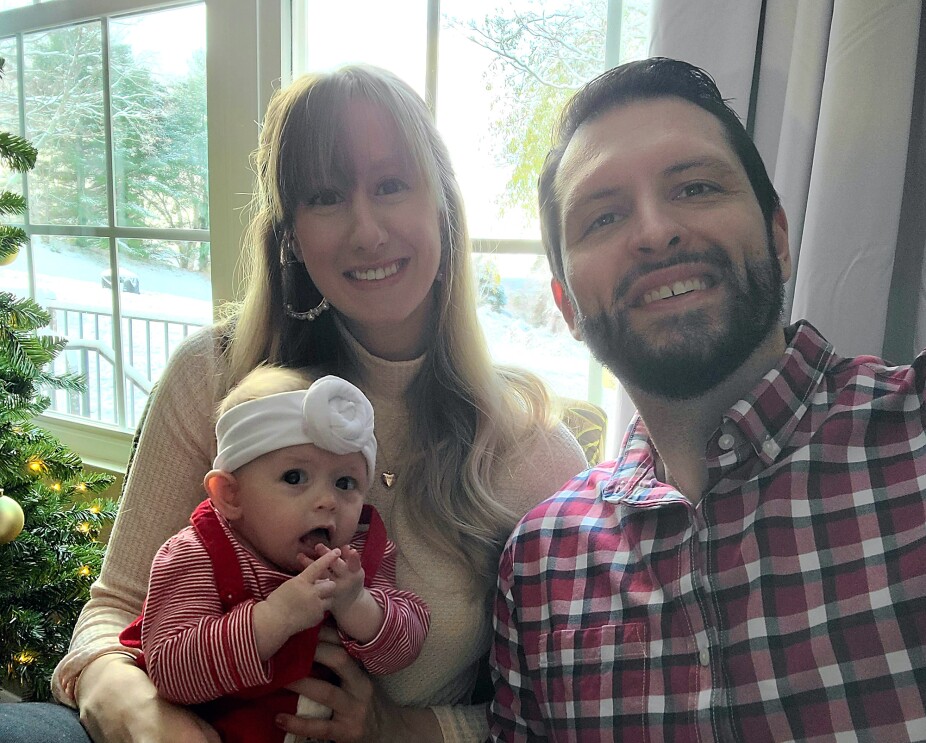 A woman and her husband pose and smile with their infant daughter