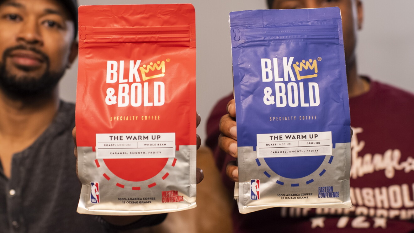 Two men hold bags of coffee labeled "BLK & Bold" and bearing the NBA logo.