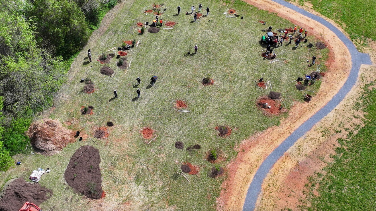 Aerial view of community members working together in a large clearing, with people gathered in groups across the grassy area