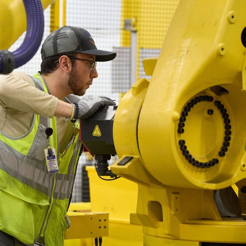 Amazon employee in safety vest maintaining yellow robotic equipment