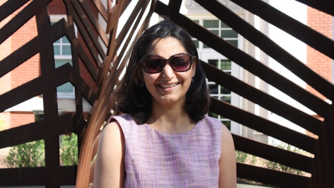 一个女人微笑的照片外的长椅上,戴着墨镜和一件紫色衣服。