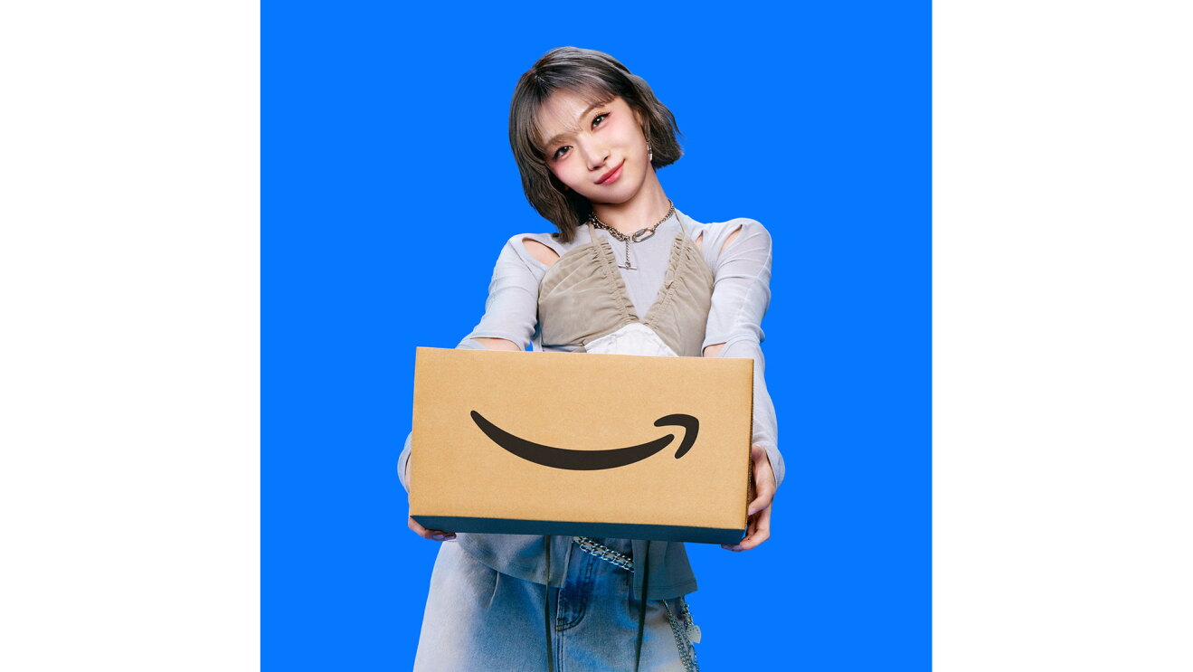 若い女性が、両手でAmazonロゴ入りダンボール箱を持って前に差し出している。