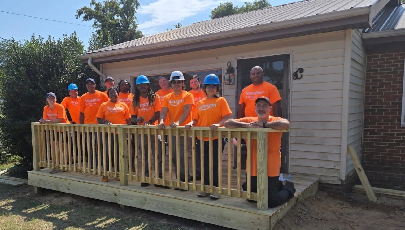  A group of Amazon employees wearing volunteer T-shirts smile while standing on a wooden deck they helped rebuild.