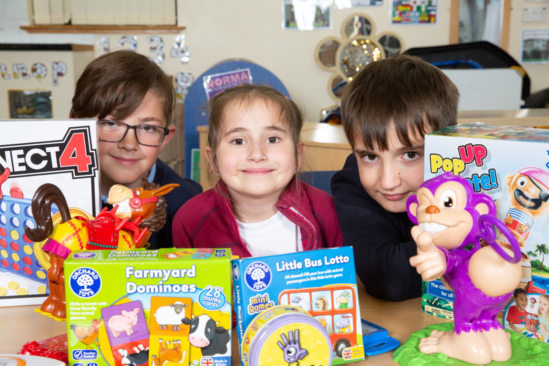 Three School children sitting behind a table full of colourful game boxes.