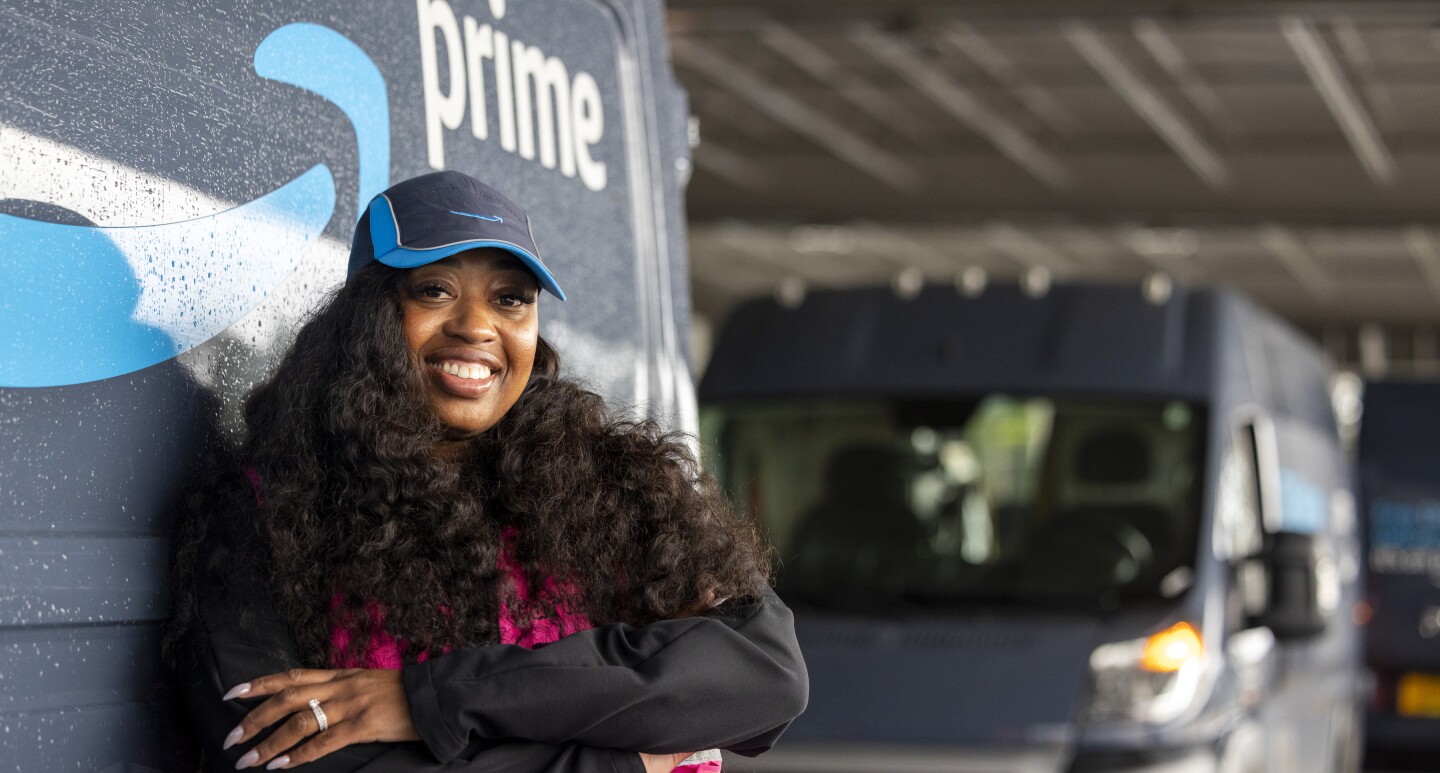 Smiling Amazon Prime delivery driver in blue cap leaning against next to an Amazon Prime truck