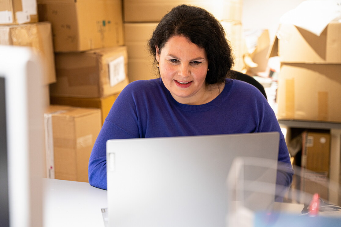Eine Frau in einem blauen Pullover schaut in einen grauen Laptop.