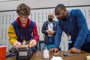 A photo of two students working on a fiber optic fusion splicer. An instructor is standing behind them.