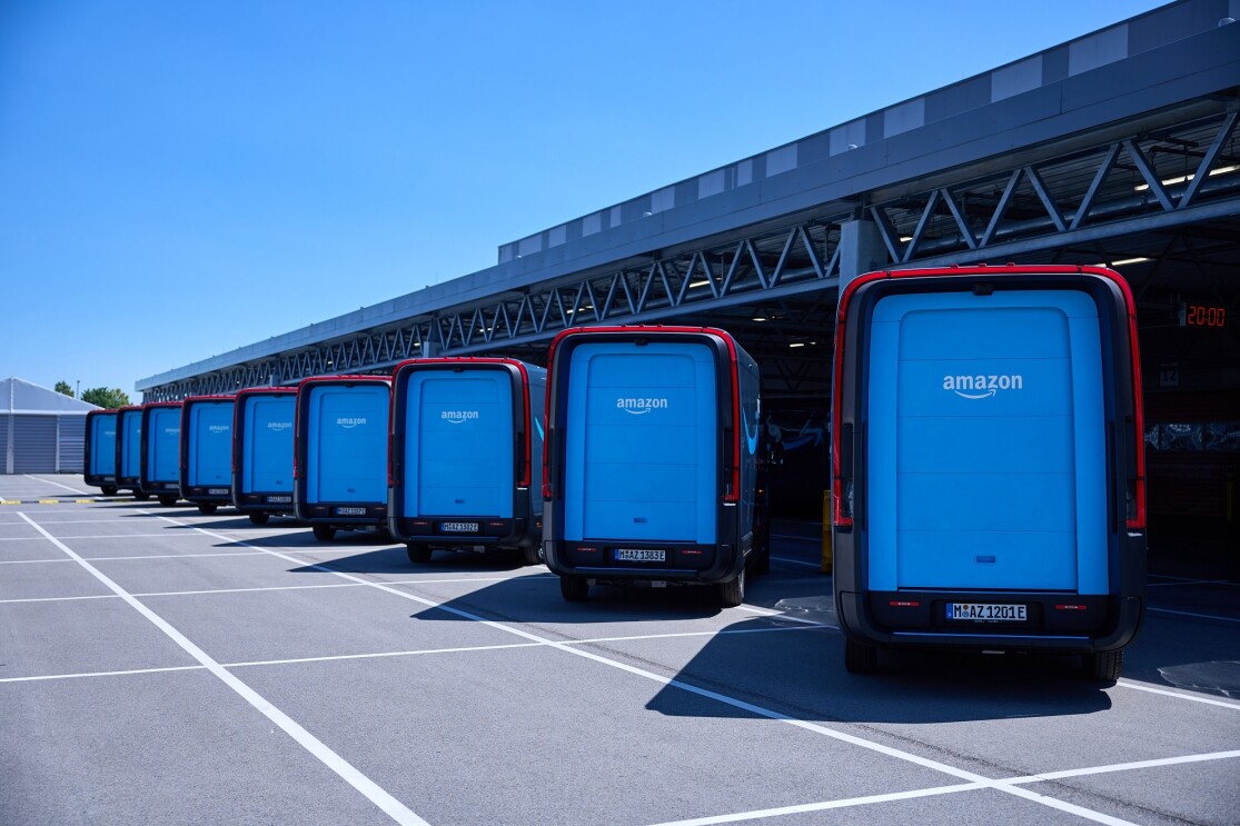 Neue Amazon Rivians von hinten, aufgereiht vor einer Halle.