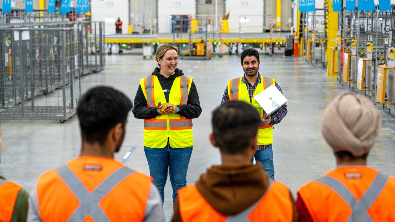 Two Amazon employees smiling and speaking to other employees in a warehouse