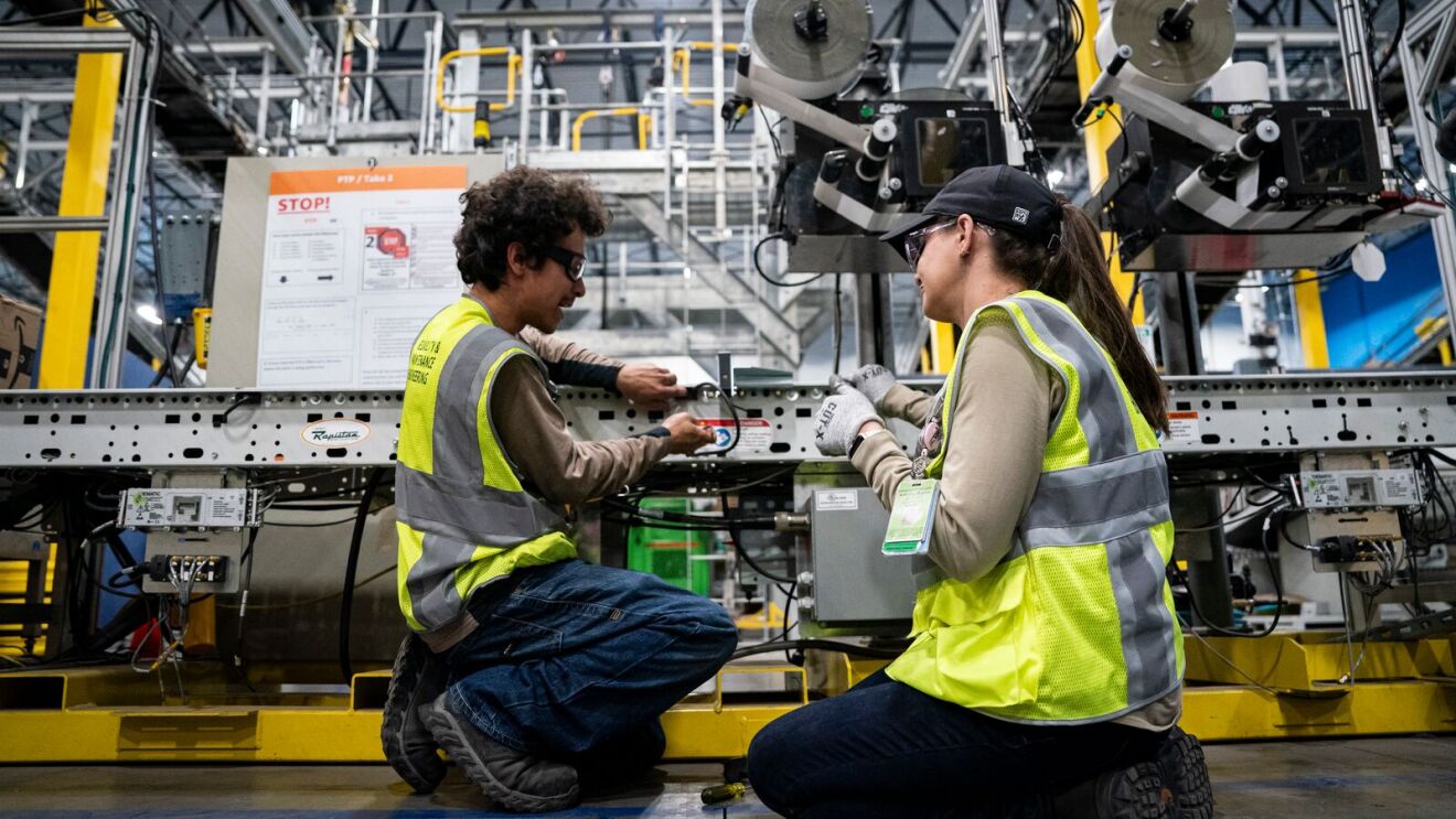 Amazon employees in safety vests collaborate on machinery maintenance