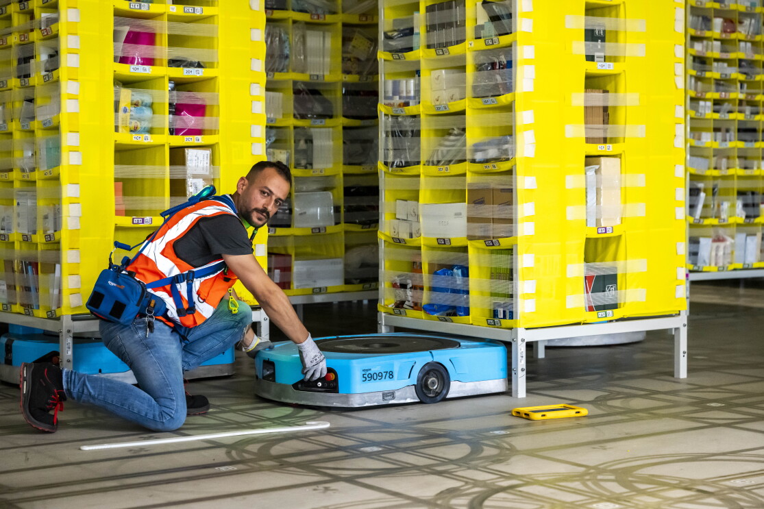 Ein Amazon Techniker kniet auf dem Boden vor einem blauen Transportroboter.