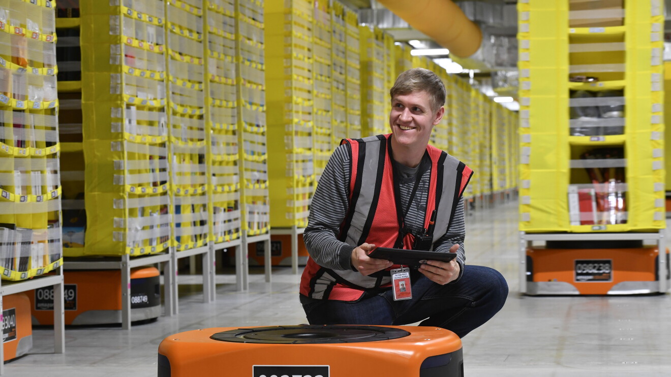 Ein Amazon Mitarbeiter im Logistikzentrum in Winsen HAM2 gemeinsam mit einem Roboter.